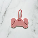 pink dog bone shaped plastic with 2 slots to carry full dog poop bags attached to a carabiner to clip onto your dog leash