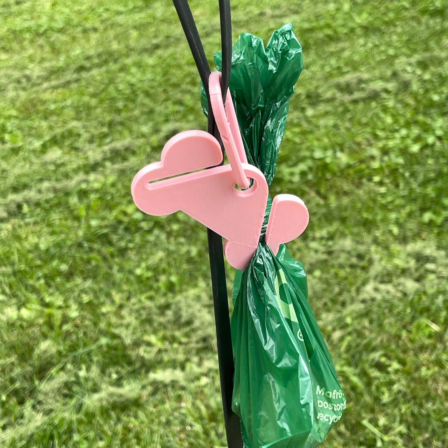 pink dog bone shaped plastic with 2 slots to carry full dog poop bags attached to a carabiner to clip onto your dog leash